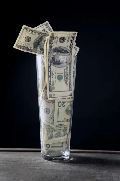 Vidro alto cheio de notas de dólar sobre preto — Fotografia de Stock