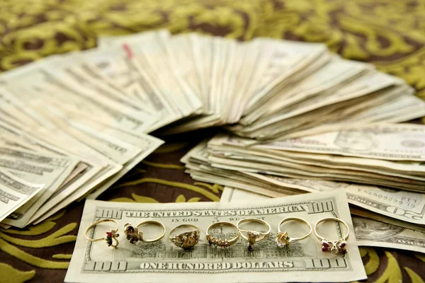 Dollar notes and gold rings over tablecloth — Stock Photo, Image