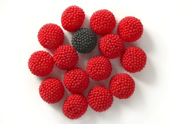 Одна черная ягода конфет, выделенная между красными ягодами — стоковое фото