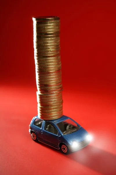 Coche de juguete con enorme columna de monedas de oro sobre rojo — Foto de Stock