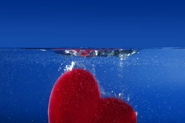 Candy forma coração vermelho afundando na água azul — Fotografia de Stock