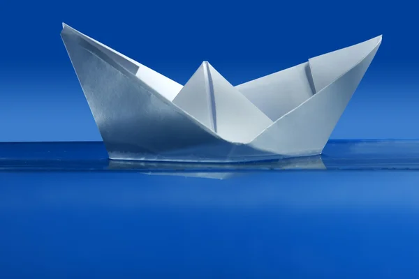 Barco de papel flotando sobre agua azul real — Foto de Stock