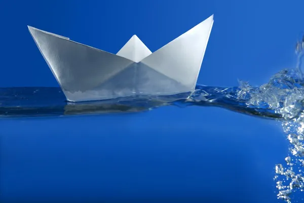 Barca di carta galleggiante sopra l'acqua reale blu — Foto Stock