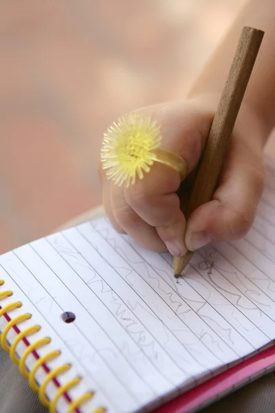Παιδιά χέρι με αστεία κίτρινο δαχτυλίδι που γράφει σε ένα σημειωματάριο — Φωτογραφία Αρχείου