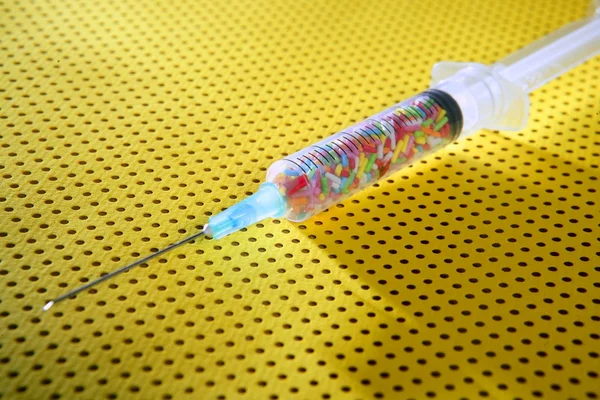 Pequena seringa de doces coloridos sobre fundo amarelo — Fotografia de Stock
