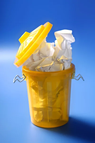 Coș de gunoi de hârtie în galben peste fundal albastru — Fotografie, imagine de stoc