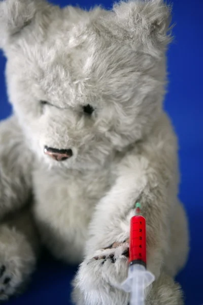 Teddy bear on the doctor, bloody vaccine syringe on its arm — Stock Photo, Image