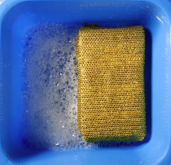 Золотая губка на голубом квадратном ведре, белая пена — стоковое фото