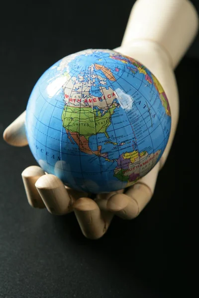 世界地图在木模特的手，黑色 backgorund — 图库照片