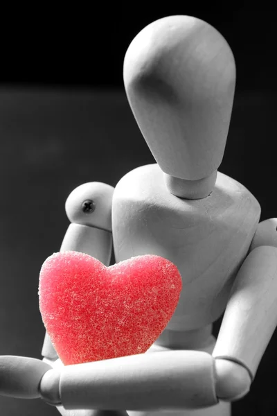 Wooden mannequin holding a red jelly heart shape — Stock Photo, Image