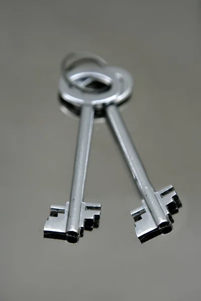 Stříbrný pár klíčů nad zrcadlo z nerezové oceli — Stock fotografie