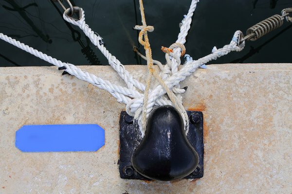 Black bollard with many nautical ropes around