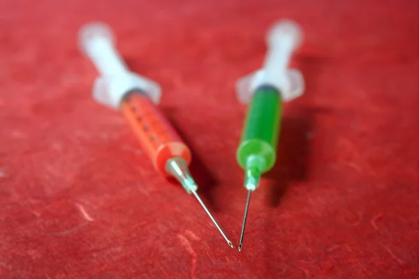 Red and green syringe over red background — Stock Photo, Image