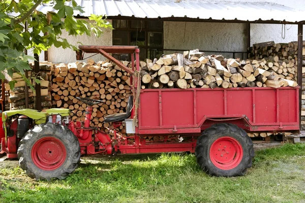 Trattore a legna da ardere di colore rosso con legna impilata — Foto Stock