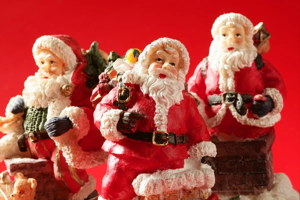 Three Santa Claus figurines over red background, studio — Stock Photo, Image