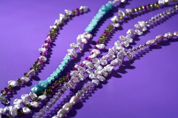 Barevné kameny šperky náhrdelníky, fialové pozadí — Stock fotografie