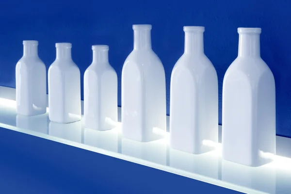 青い背景の棚の上の白ボトル行 — ストック写真