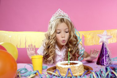 Happy little blond girl blowing cake candle in a birthday party clipart