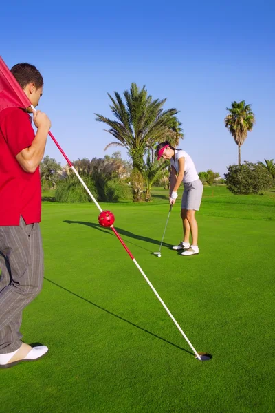 Golf-Frau setzt Gol-Ball und Mann hält Fahne — Stockfoto