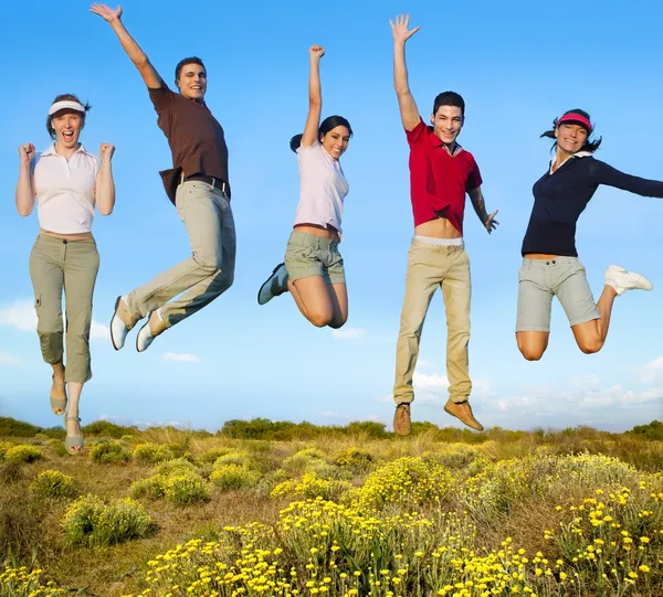 Jumping young happy group on yellow flowers — Stock Photo, Image