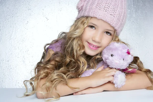 Зимняя модная шапочка маленькая девочка обнимает плюшевого медведя улыбаясь — стоковое фото