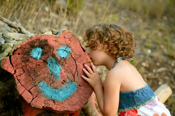 Girl kiss a cutted trunk with happy face draw — Stock Photo, Image