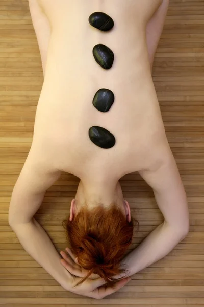 Mulher bonita relaxar pedras pretas nas costas — Fotografia de Stock