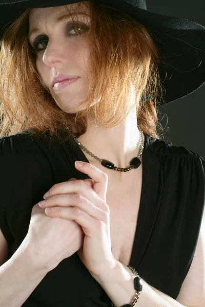 Γυναίκα όμορφη κοκκινομάλλα σε μαύρο, καπέλο και κοσμήματα — Φωτογραφία Αρχείου