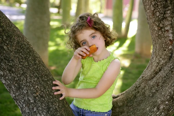 Beautiful little girl eating biscuit over tree — Stock Photo, Image