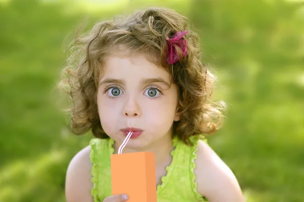 Маленькая девочка пьет сок из апельсинового брика — стоковое фото