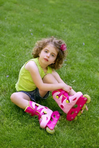 Klein meisje zitten op het gras met rolschaatsen — Stockfoto