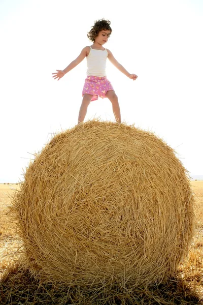 Menina jogando sobre o fardo seco de trigo redondo — Fotografia de Stock