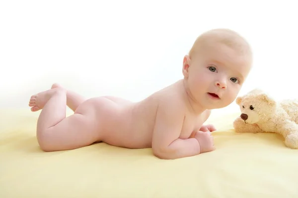 Малыш играет в плюшевого мишку лежа на кровати — стоковое фото