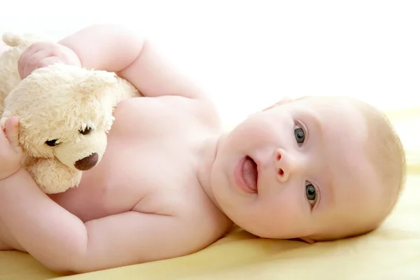 Bebê jogando ursinho deitado na cama — Fotografia de Stock