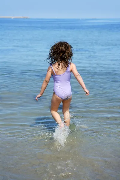 Брюнетка маленькая девочка бежит в пляжную воду — стоковое фото