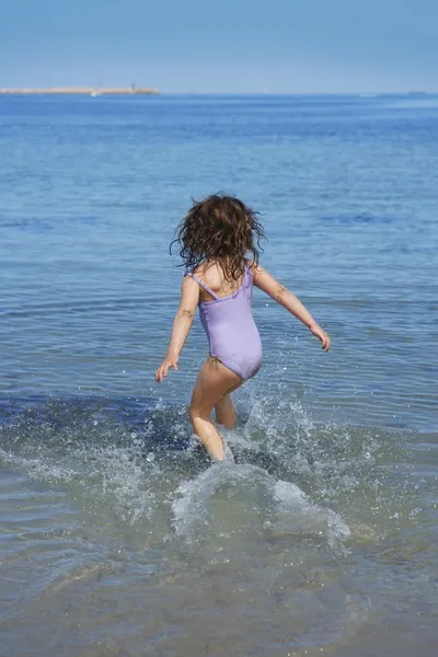 Brunette little girl running into beach water — Stock Photo, Image