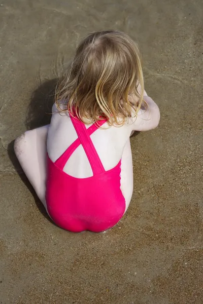 Blond little girl swimsuit back playing on beach sand — Stock Photo, Image
