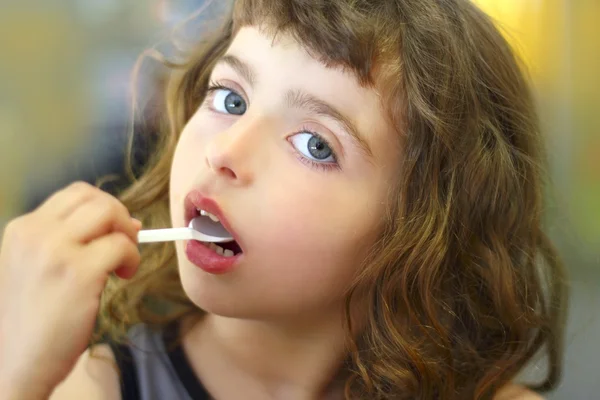 Malá brunetka jíst, hrát plastovou lžící — Stock fotografie