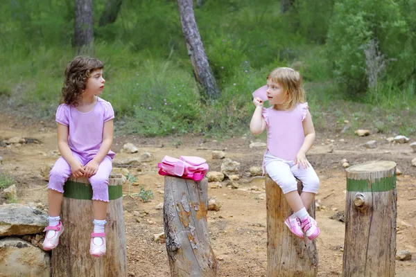 Two little girls sit on forest park tree trunks — Stockfoto