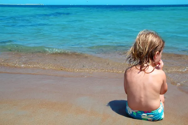 Pequena menina loira sentar-se na praia olhando oceano — Fotografia de Stock