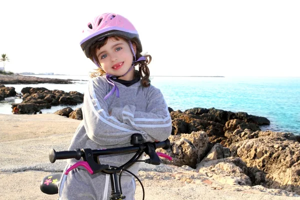 Fiets weinig gelukkige meisje roze helm in rotsachtige zee — Stockfoto