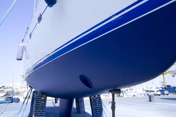 Парусная лодка синего цвета, выброшенная на берег для покраски — стоковое фото