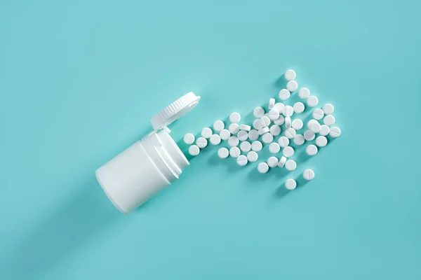 Bottle with white pills coming out over green background — Stock Photo, Image