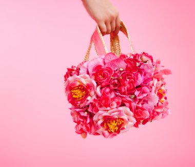 Red flowers bag in woman hand on pink background clipart