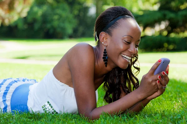 Adolescente menina negra usando um telefone, deitado na grama — Fotografia de Stock