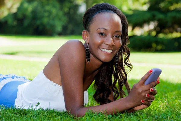 Teenage black girl using a cellphone, lying on the grass — Stock Photo, Image