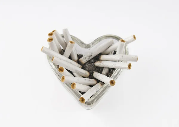 Corazón de cristal con colillas de cigarrillo sobre un fondo blanco — Foto de Stock