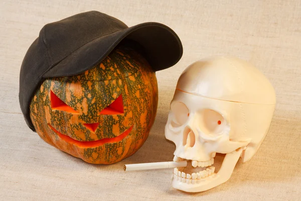 The cheerful halloween pumpkin and skull with cigarette — Stock Photo, Image