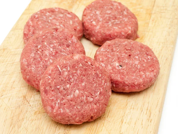 Hambúrgueres de carne crua fecham em um conselho Imagem De Stock