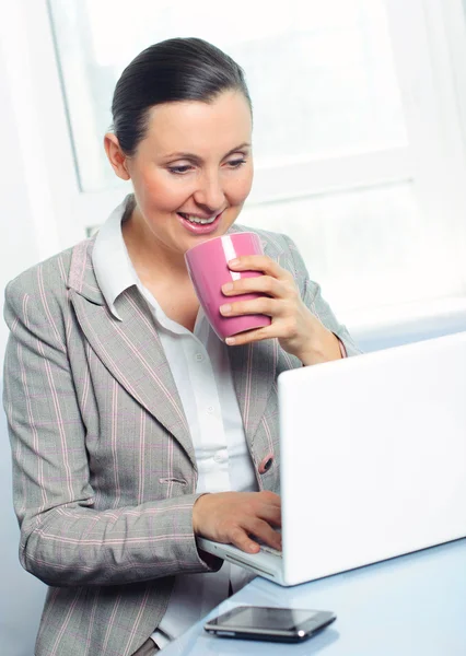 Sorridente giovane donna d'affari con tazza utilizzando il computer portatile — Foto Stock